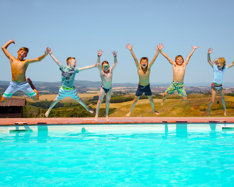 Kinder und Jugendliche springen gemeinsam am Pool in die Luft und haben Spaß im Urlaub.
