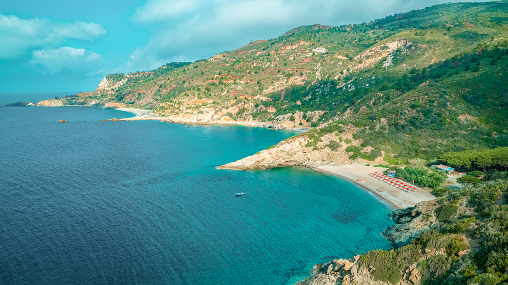 Weitläufige Küstenlandschaft mit steilen Hängen und tiefblauem Meer entlang einer geschützten Bucht.