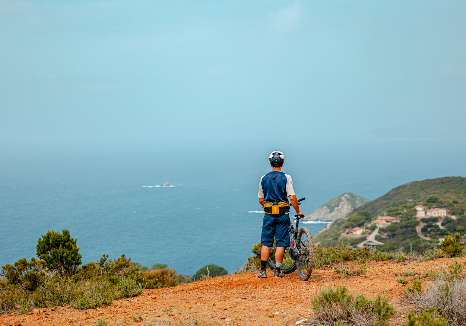 Radfahrerin auf einem Naturweg mit Blick auf die Küstenlandschaft und das Meer.
