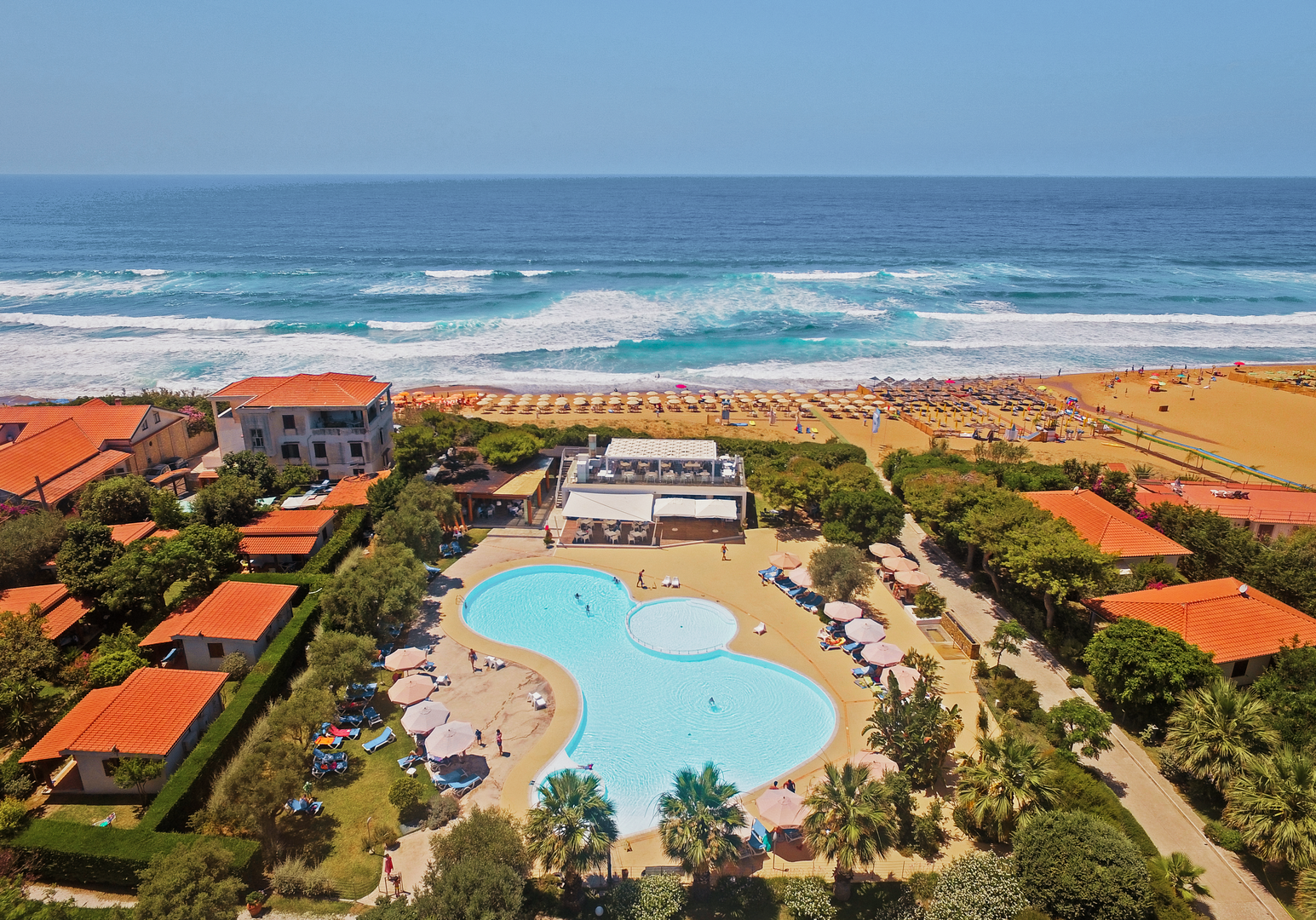 Luftaufnahme einer Ferienanlage mit Poollandschaft und direkter Lage am Sandstrand.