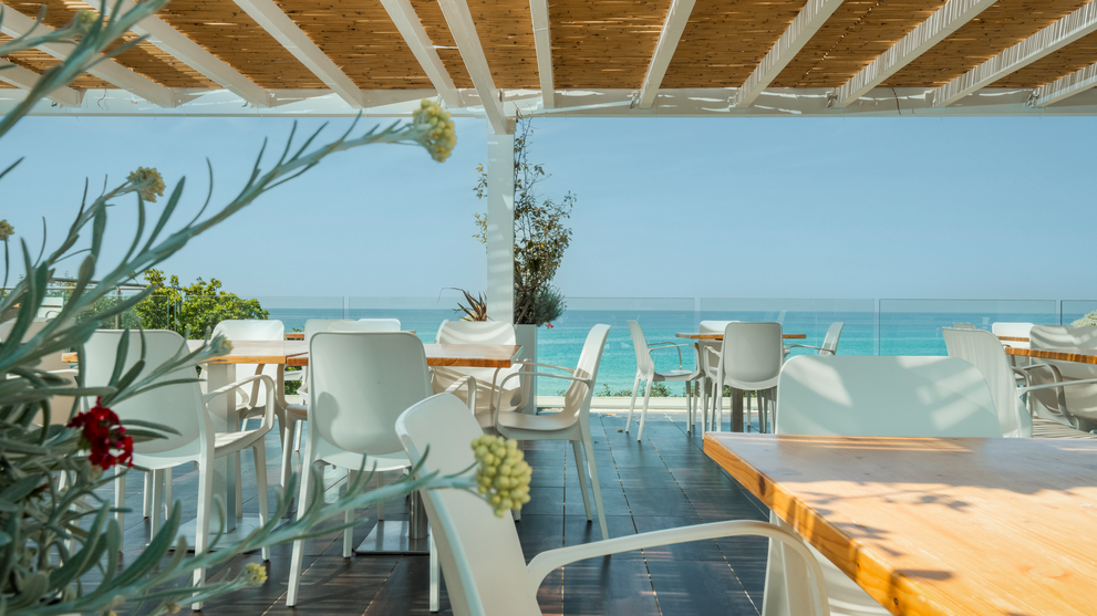Gedeckte Tische auf einer Terrasse mit Panoramablick auf die Küste und das Meer.