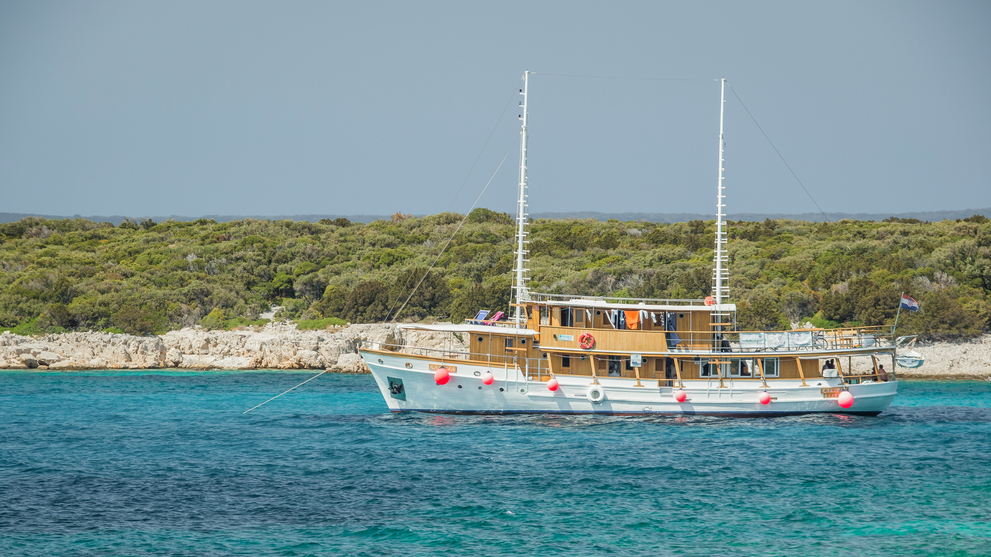 Traditioneller Motorsegler ankert in einer türkisfarbenen Bucht vor einer grünen Insel.