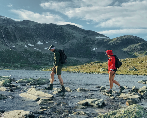 Zwei Personen wandern durch eine offene Gebirgslandschaft mit Blick auf Seen und Berge.