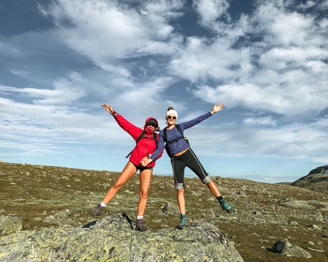 Zwei Wandernde posieren auf einem Bergplateau vor bewölktem Himmel.