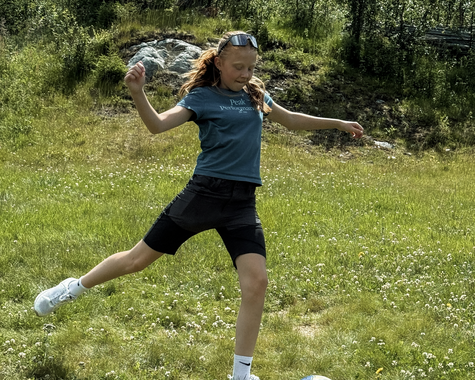 Kind spielt Fußball auf einer Wiese in naturnaher Umgebung.