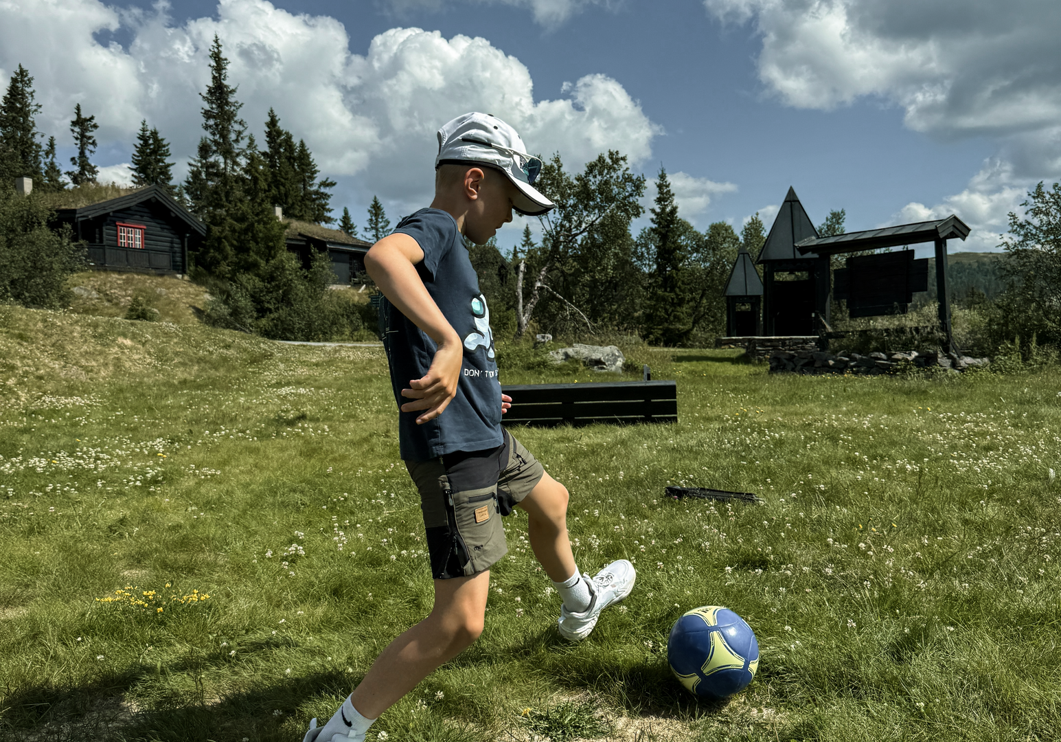 Kind balanciert einen Fußball auf einer Wiese unter wolkigem Himmel.