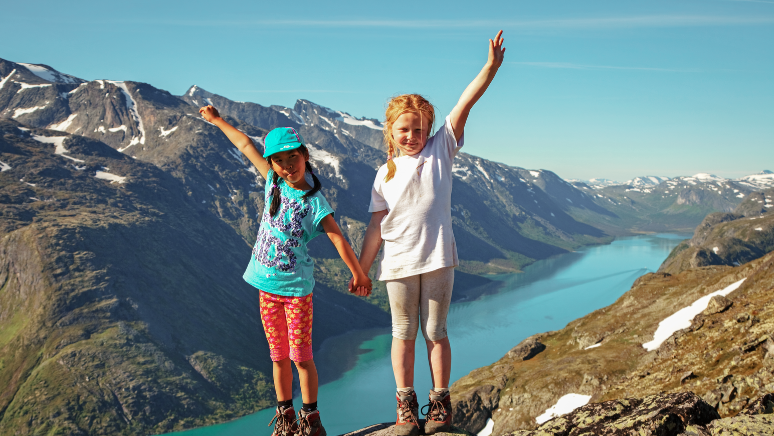 Kinder stehen auf einem Aussichtspunkt mit Blick auf eine Berglandschaft.