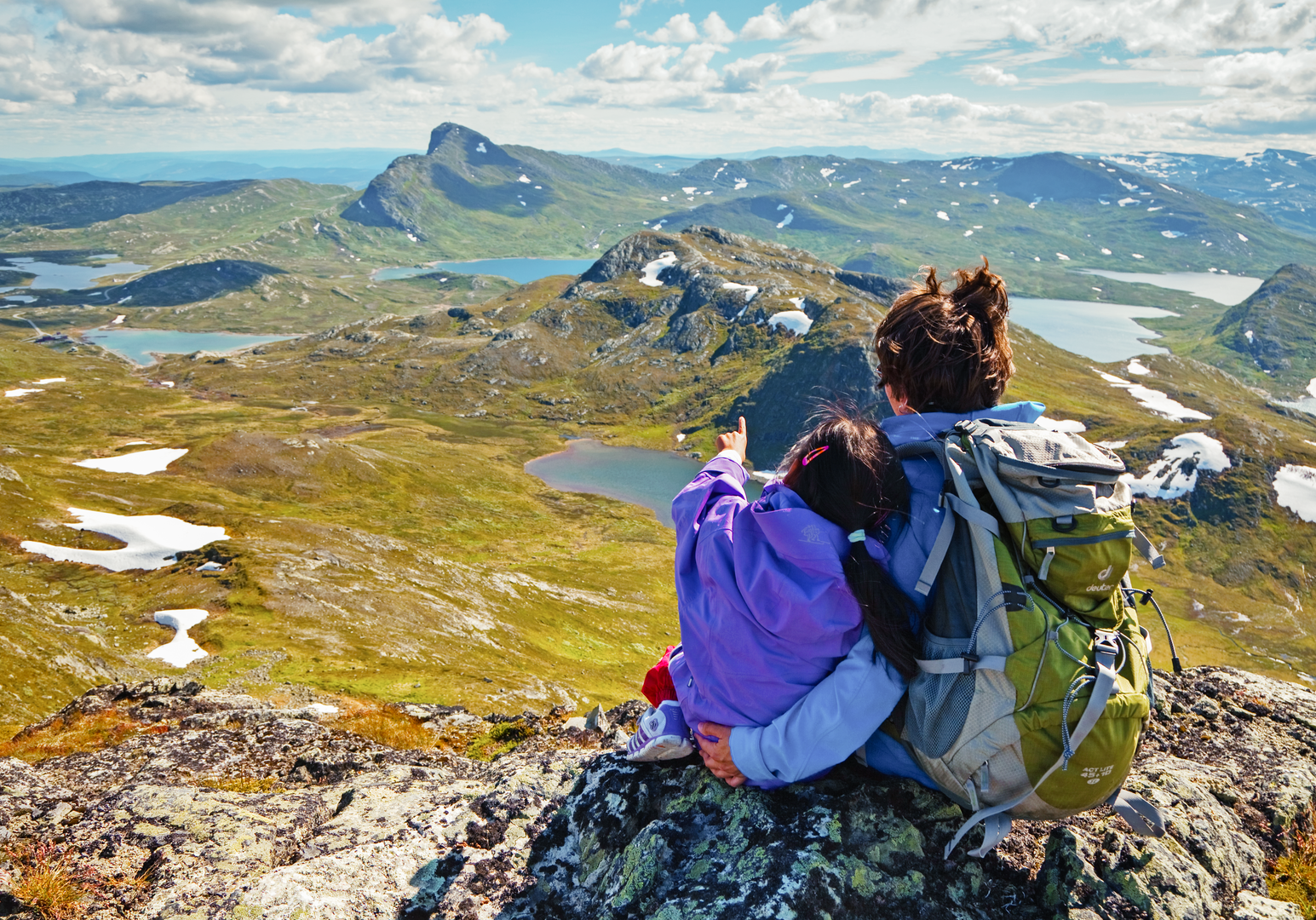 Zwei Personen sitzen auf einem Felsen und genießen die Aussicht auf Berge und Seen.
